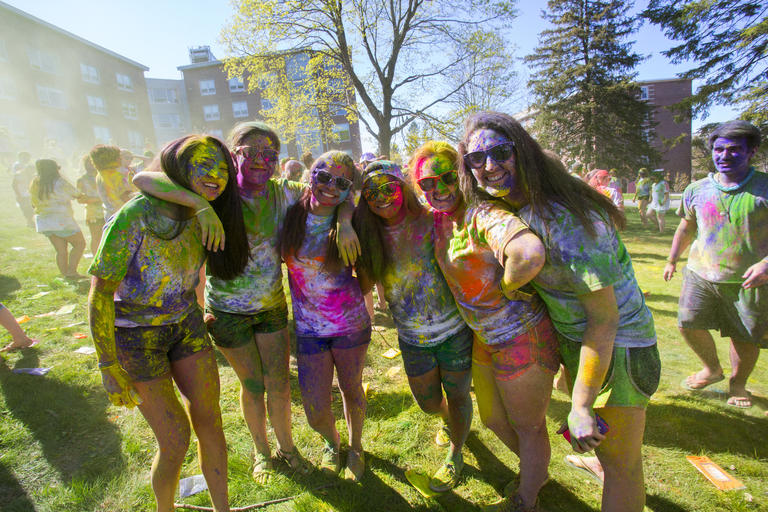 A group of students on a bright sunny day just having gone through an event where they had multiple paint colors sprayed on them