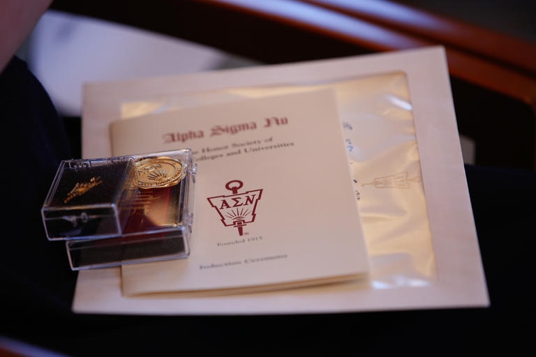Alpha Sigma Nu pin with a copy of the event program