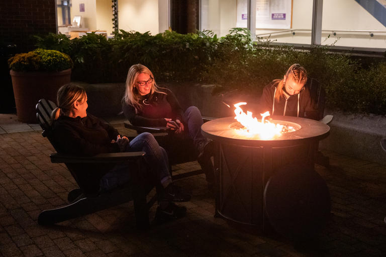 Three people sitting around firepit and night