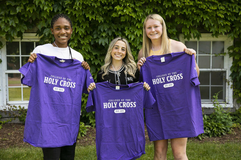 Three students holding up their Holy Cross t-shirts