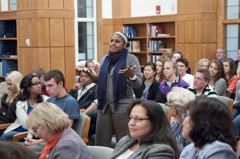 A student stands to ask a question among the filled seats of a lecture in Rehm Library.