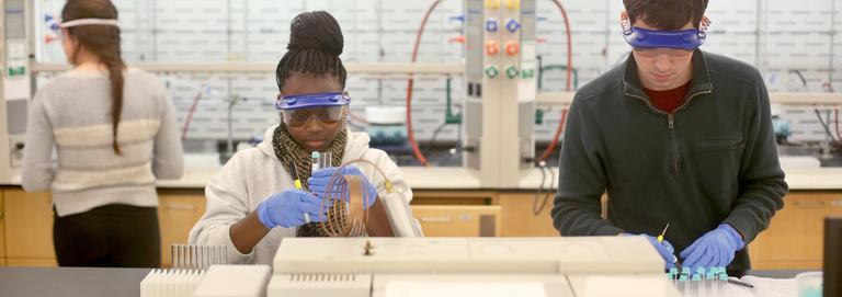two students working in a lab wearing goggles