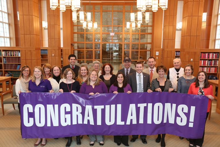 Group of Admissions staff people holding up purple sign that reads, "Congratulations"