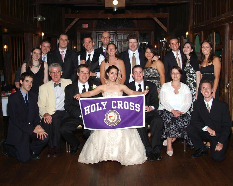 Bride and groom holding up Holy Cross banner and surrounded by wedding guests