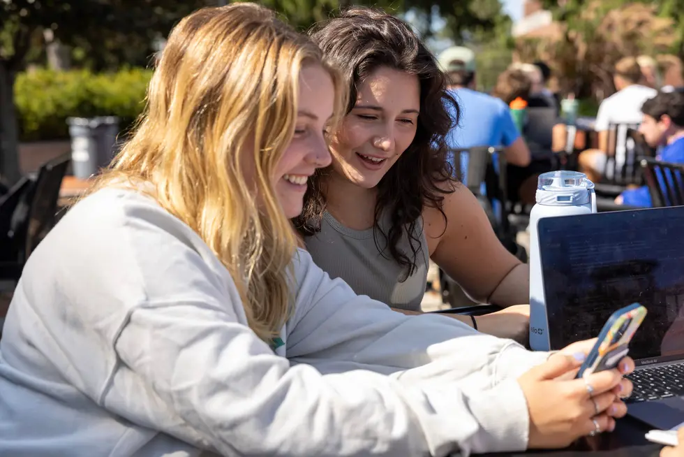 Two students smiling, looking at a phone