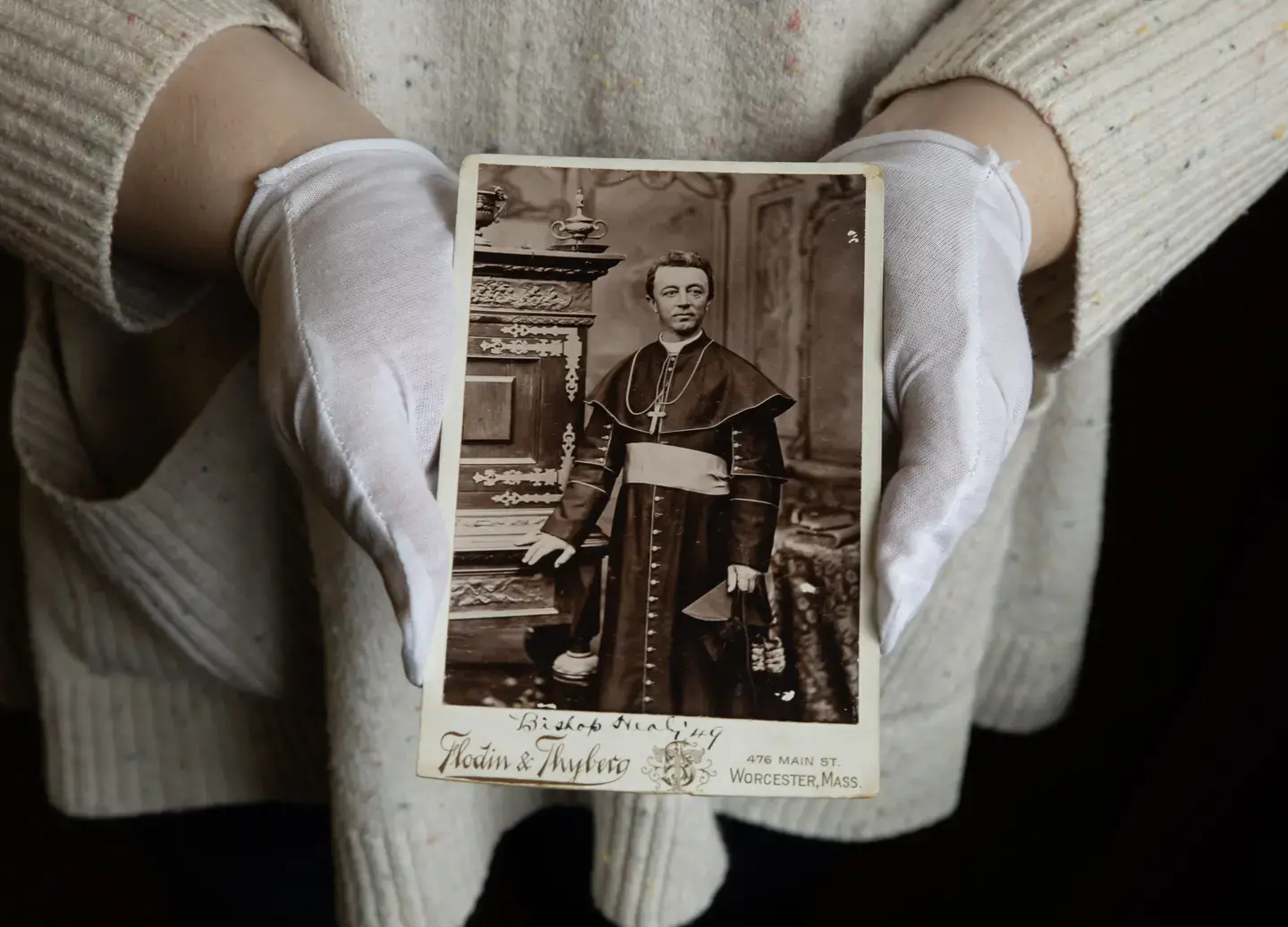 Gloved hands holding a historic photo of a bishop