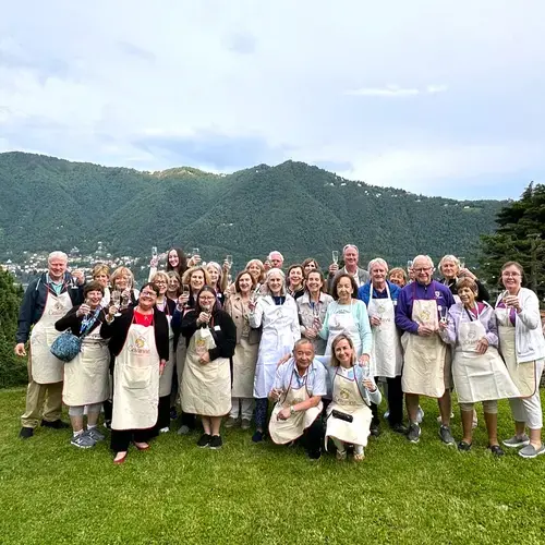a group of alumni wearing aprons toasting the camera in italy