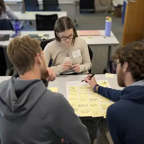Three people work at a table on a social entrepreneurship project at Holy Cross