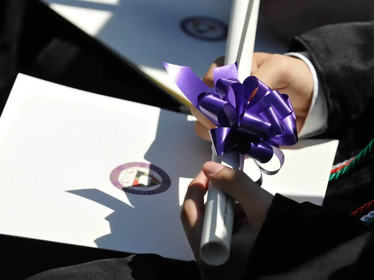 A Holy Cross graduate holding their diploma. 