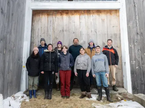Group of students and a professor standing against a barn door