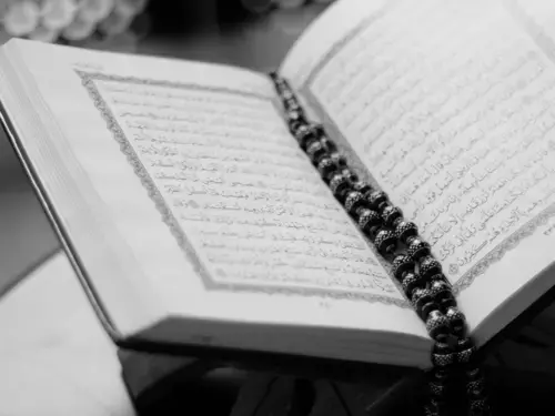 A black-and-white photograph of an open Quran resting on a wooden book stand