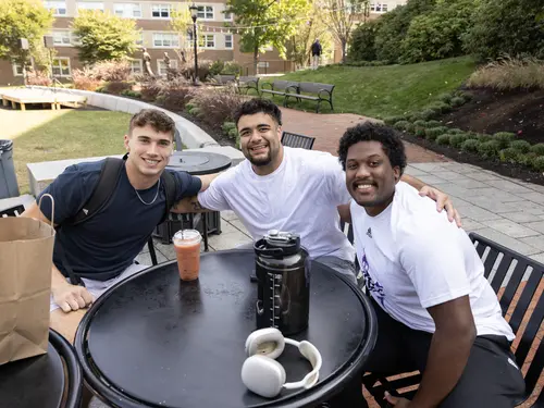 A group of students gathered around a table on the Hoval at Holy Cross pose for a photo