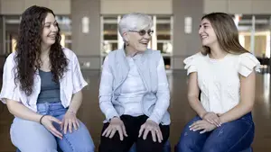 Two female graduating seniors talk with a female former professor.