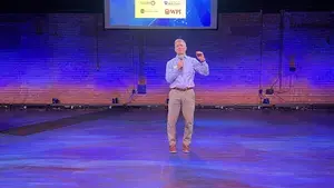 Businessman addressing crowd with a microphone in front of a screen that has "WooTank" projected on it.