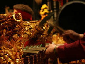 An image of an individual’s hands as they are playing a gold embellished Gamelan instrument.