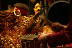 An image of an individual’s hands as they are playing a gold embellished Gamelan instrument