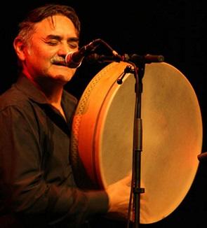 A man playing a large frame drum in front of a microphone.