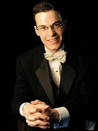 Headshot of Nathan Laube, organist, dressed in black tuxedo, leaning forward, smiling