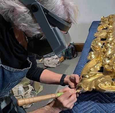 Conservator working to restore the gilding on carved wooden frame.