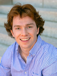 young man sitting on stairs he has red hair and light blue shirt smiling at the camera