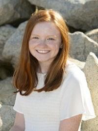 close up of a young woman with long red hair sitting on rocks outside smiling at the camera