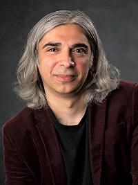 close up of faculty member with medium length hair smiling at the camera with a dark shirt and blazer on