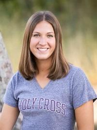 young woman outside wearing a gray Holy Cross tshirt with shoulder length hair smiling