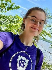 young woman wearing a purple Holy Cross shirt smiling down at the camera