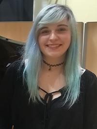 close up of student with blue hair with black top smiling at the camera
