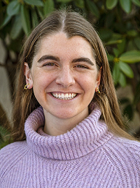 close up of a young woman with long brown hair wearing a light purple sweater smiling at the camera