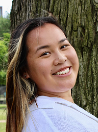 close up of a young woman with long hair standing in front of a tree smiling at the camera