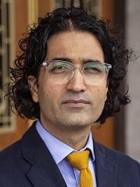 close up of a male faculty member with dark hair wearing glasses a suit coat and tie