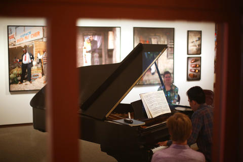 a glimpse through a window of a person playing piano in an art gallery
