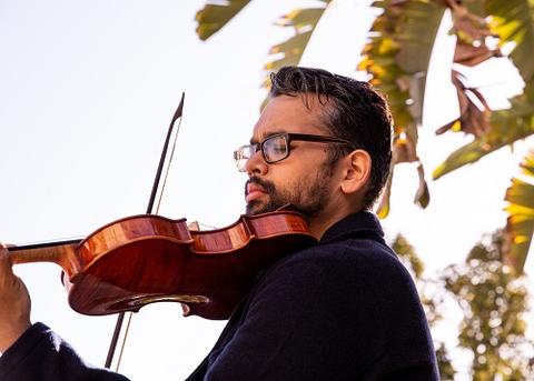 A man playing the violin in an outdoor setting with trees behind him.