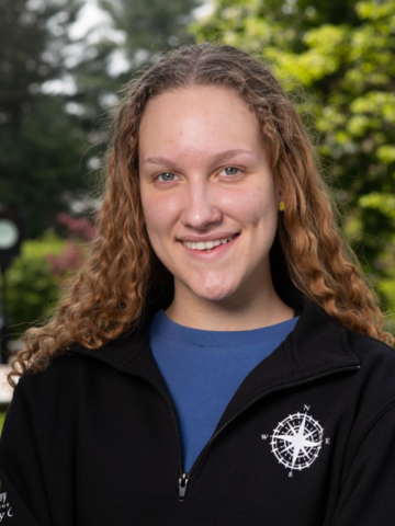 Headshot of Amanda who has light brown curly hair and is wearing a black Holy Cross sweater with a blue shirt underneath.