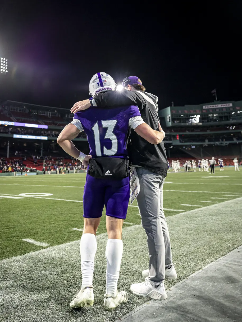 A Holy Cross football player and coach share words before a possession during a game at Fenway Park