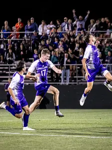 Holy Cross men's soccer celebrates scoring a goal with a sold out crowd behind three players cheering on the team.