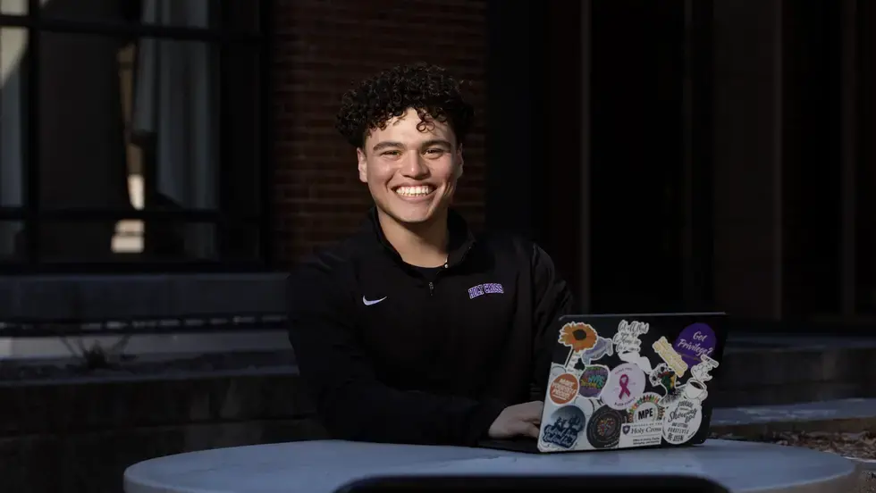 Young Hispanic male student sitting at a table with a laptop.