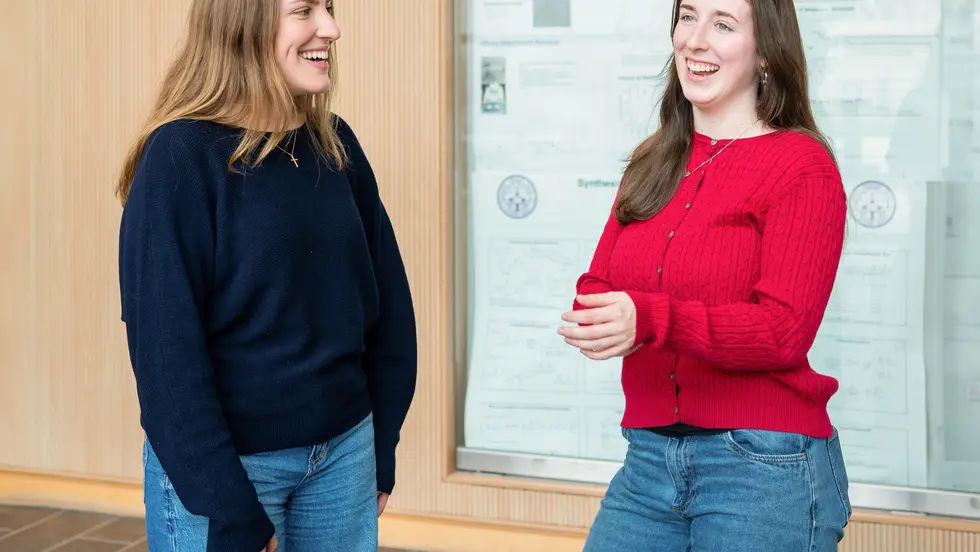 Two women in conversation in front of a whiteboard.