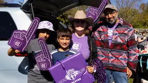 a family of 4 decked out in purple holding large purple foam fingers