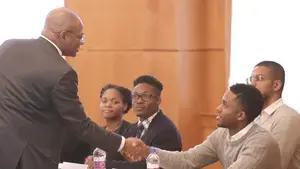 a man shaking hands with a young man sitting at a table
