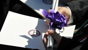 A Holy Cross graduate holding their diploma. 