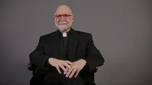 William E. Stempsey, S.J. sits in a chair for a portrait photo. 
