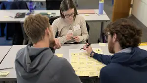 Three people work at a table on a social entrepreneurship project at Holy Cross