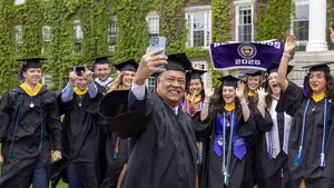 Graduates pose for a photograph with College President Vincent Rougeau in front of Fenwick Hall