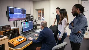 Three people stand behind one professor in the Brooks Recording Studio at Holy Cross