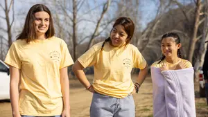Three students stand on a riverbank, one in a towel, after the river swim