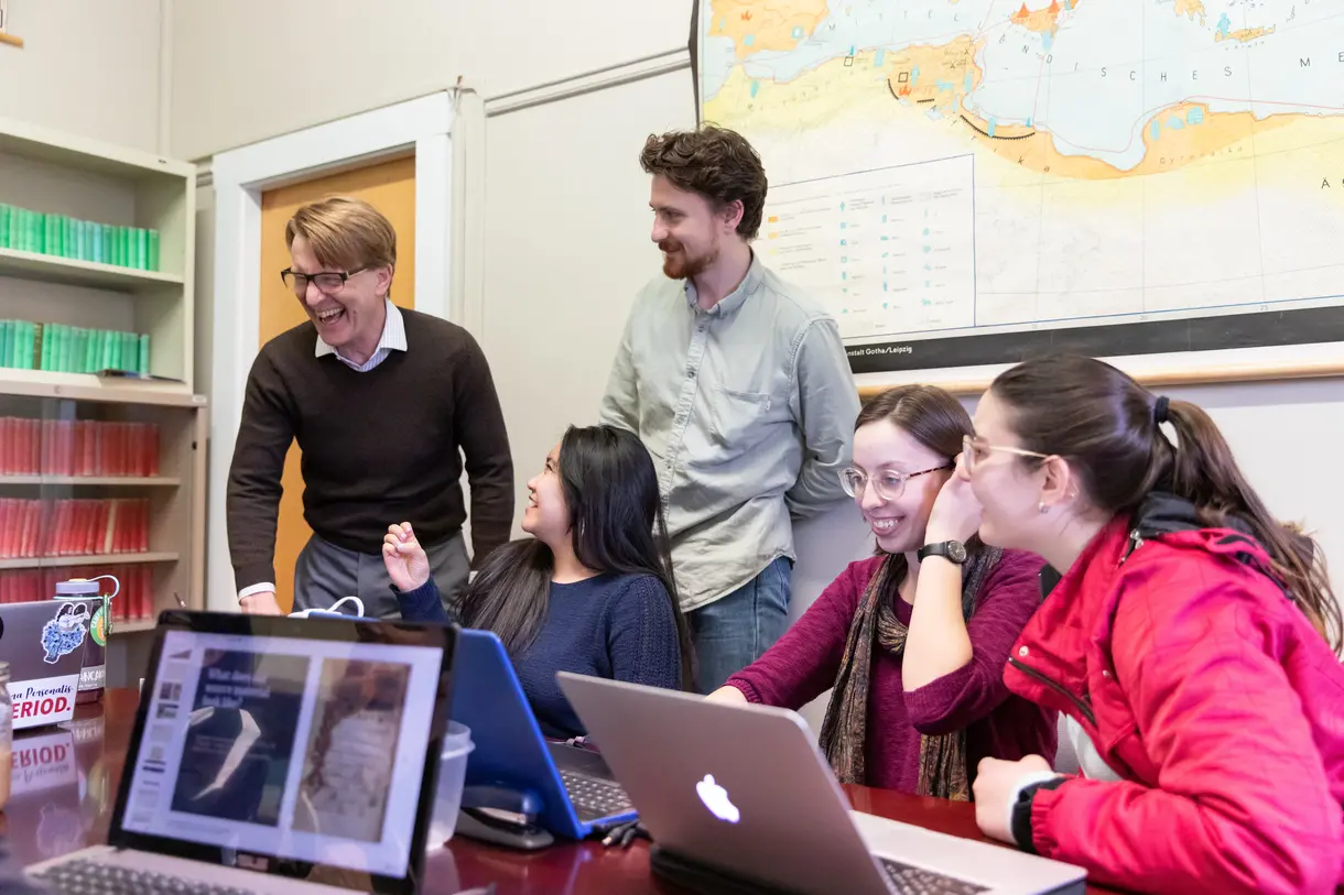 Students and faculty member sitting at a table with computers.